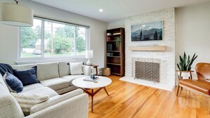 A modern living room with a sofa, a round coffee table, a fireplace, and a bookshelf. - Cozy Modern Single Family 5BD 2BA Home (Falls Church)