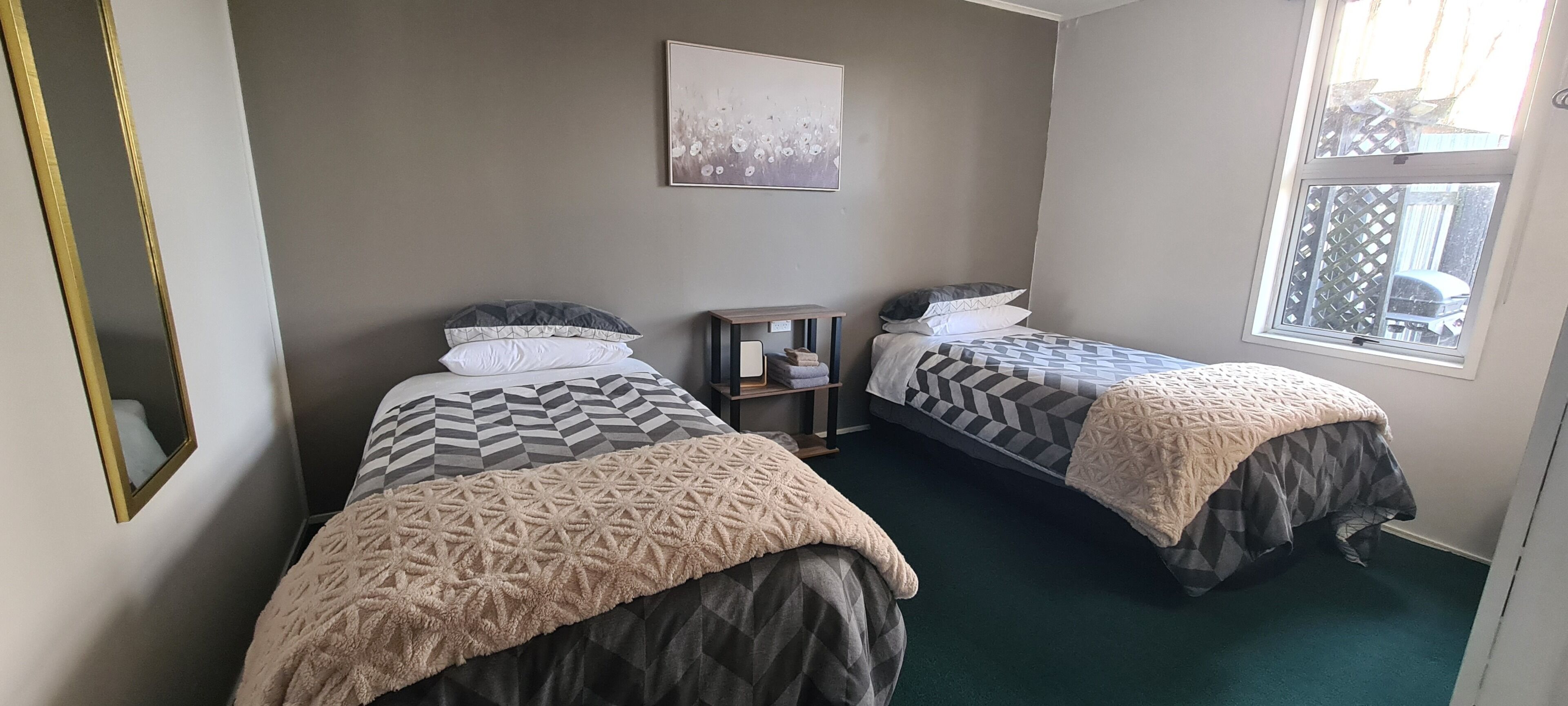 Quarto com duas camas, uma mesa de cabeceira, uma janela e um espelho.