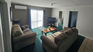 A living room with two sofas, a coffee table, a television, and a window with curtains. - Kawakawa Cottage - lovely rural outlook. Convenient location to Manfield Park  (Feilding)
