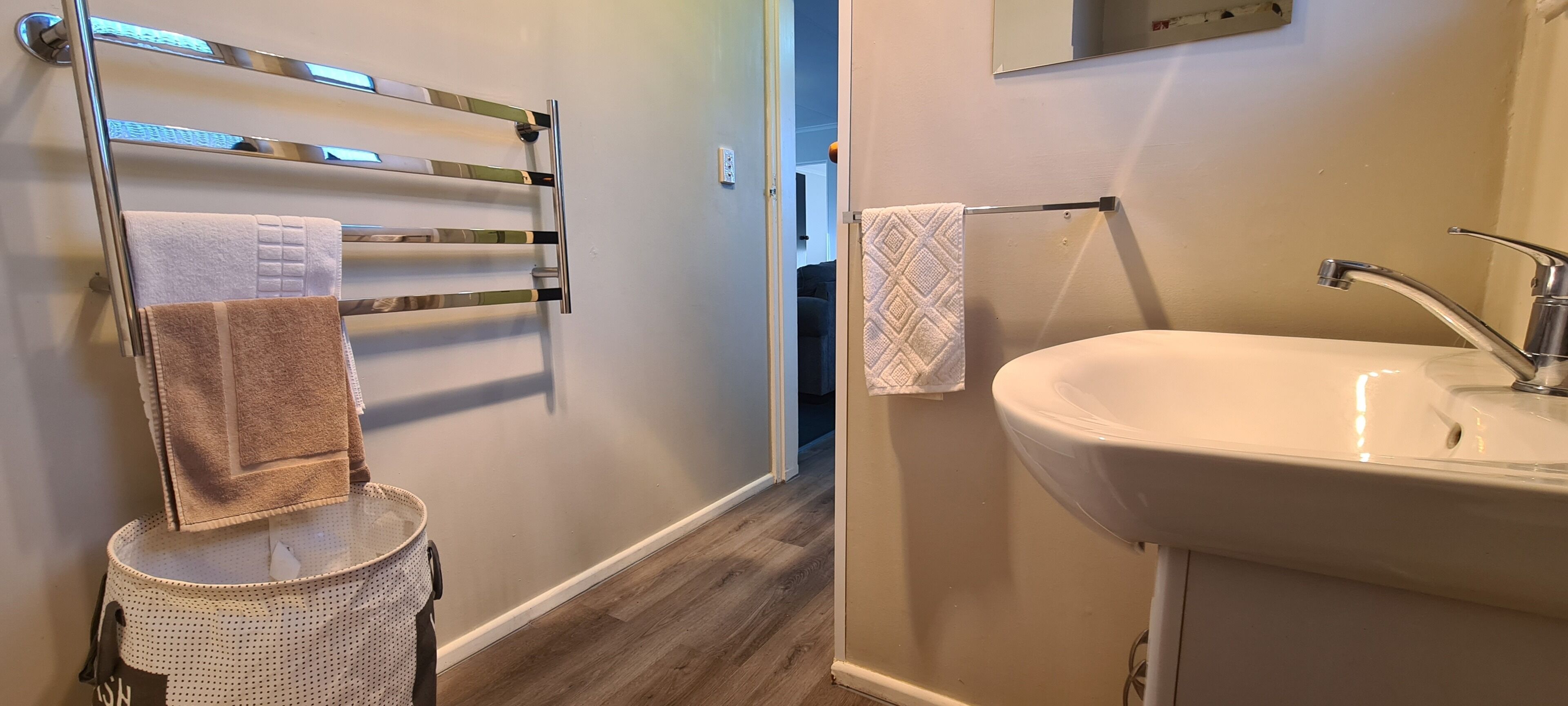 Un bagno con un lavandino bianco, un portascopino con diversi asciugamani e un piccolo cestino.