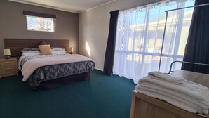 A bedroom with a bed, bedside tables, a window, a curtain, and a stack of towels. - Kawakawa Cottage - lovely rural outlook. Convenient location to Manfield Park  (Feilding)
