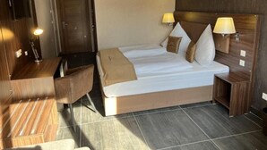 A hotel room with a bed, bedside lamps, a desk, and a chair. - Hotel Pasa Paradies (Hanau)