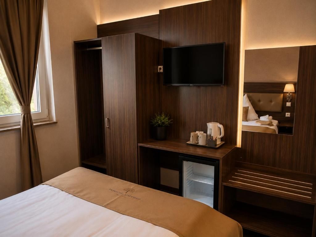 A hotel room with a bed, a TV mounted on the wall, a desk with a plant, and a small refrigerator.
