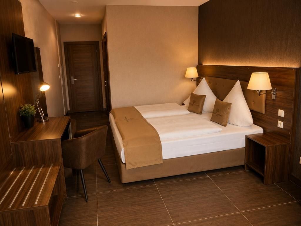 A hotel room with a double bed, two bedside tables with lamps, a desk with a chair, and a TV mounted on the wall.