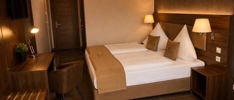 A hotel room with a double bed, two bedside tables with lamps, a desk with a chair, and a TV mounted on the wall.