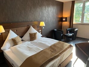 A hotel room with a bed, two bedside lamps, a chair, and a small table. - Hotel Pasa Paradies (Hanau)