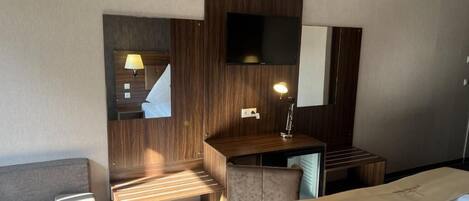 Habitación de hotel con cama, escritorio, silla, televisor montado en la pared y lámpara.