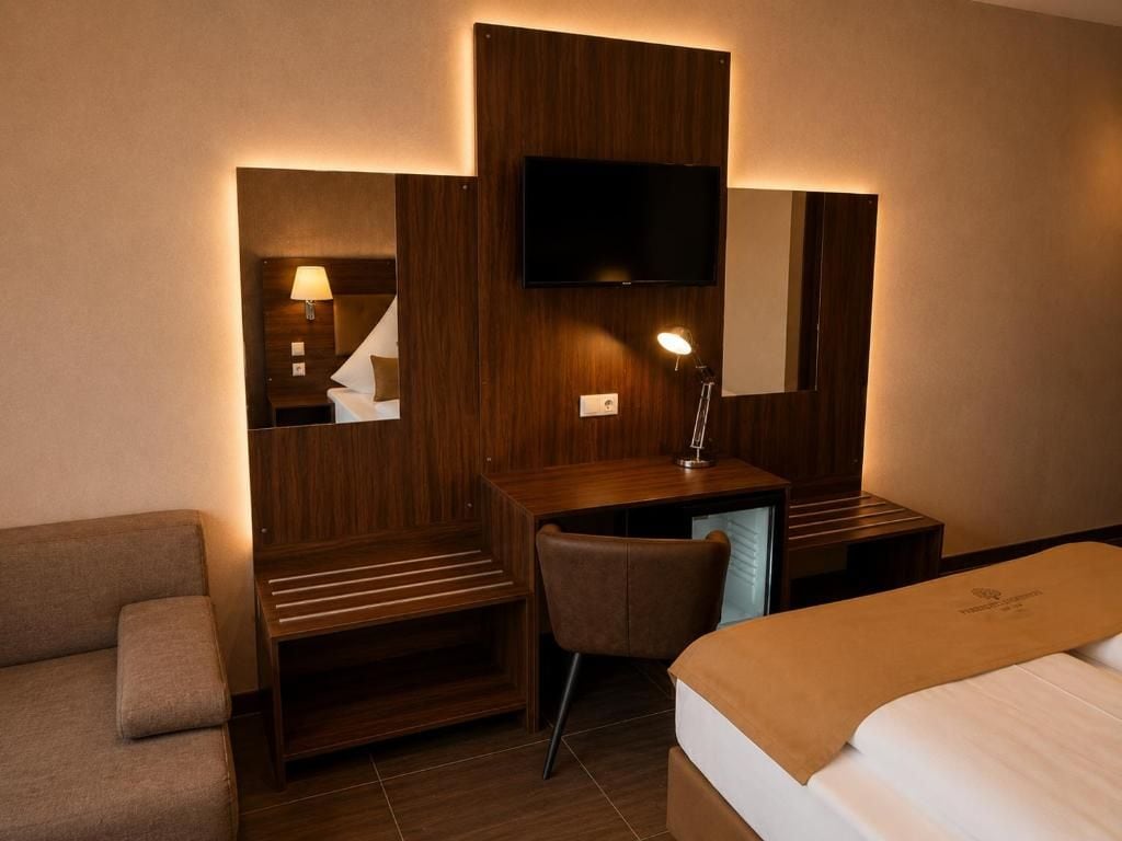 A hotel room with a bed, a desk, a chair, a TV, and a lamp.