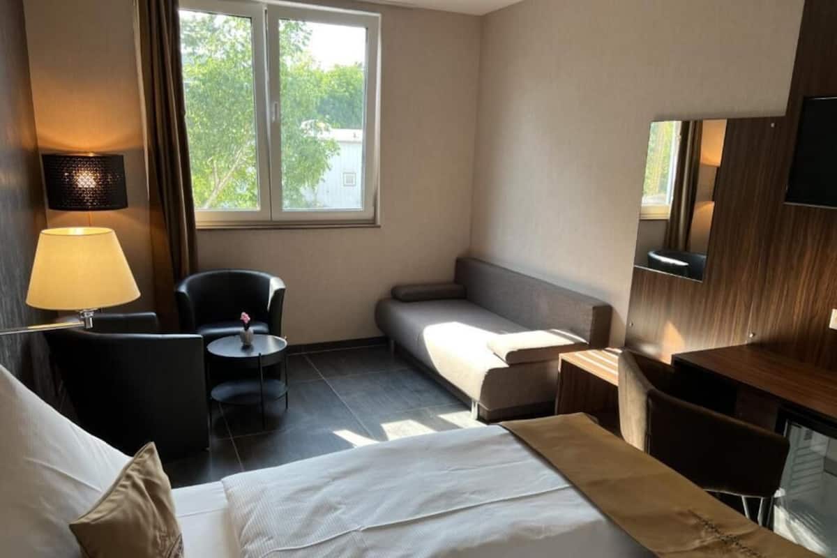 Hotellihuone, jossa on sänky, työpöytä, tuoli, sohva, lamppu ja televisio.