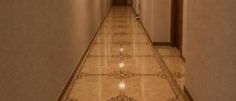 A hallway with patterned flooring, a wooden door at the end, and a light fixture on the ceiling.