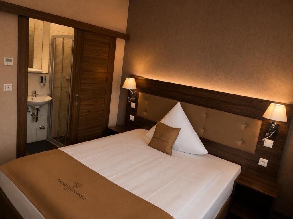 A hotel room with a bed, bedside lamps, a headboard, and a bathroom visible through an open door.