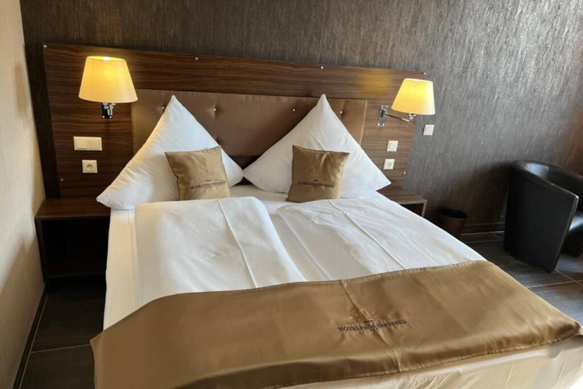 Hotellihuone, jossa on suuri sänky, kaksi yöpöytävalaisinta ja puinen sängynpääty.