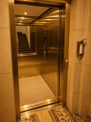 An elevator with a metallic interior, a visible emergency phone, and a carpeted floor. - Hotel am Rondo (Hanau)