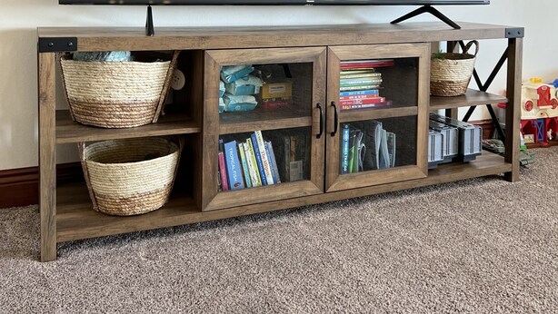 Een houten tv-meubel met manden en boeken, een flatscreen televisie erboven en een vloerbedekking.
