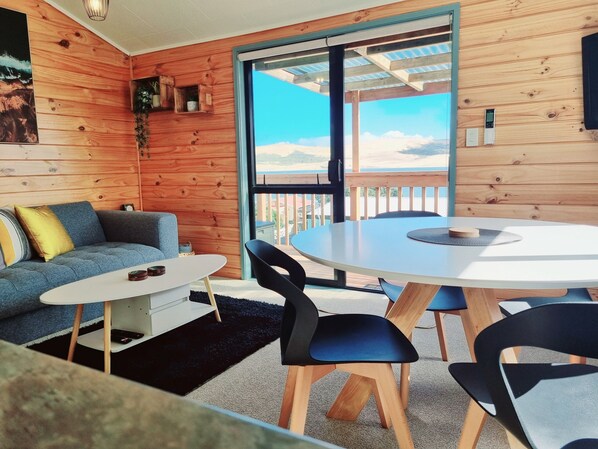 A cozy room with a wooden interior, a round table with chairs, a sofa, and a view of the outdoors.