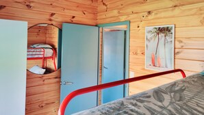 A wooden cabin interior with a bunk bed, a blue door, and a wall-mounted picture of palm trees.