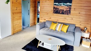 A cozy room with a grey sofa, a small white table, and a wooden wall with a framed picture.