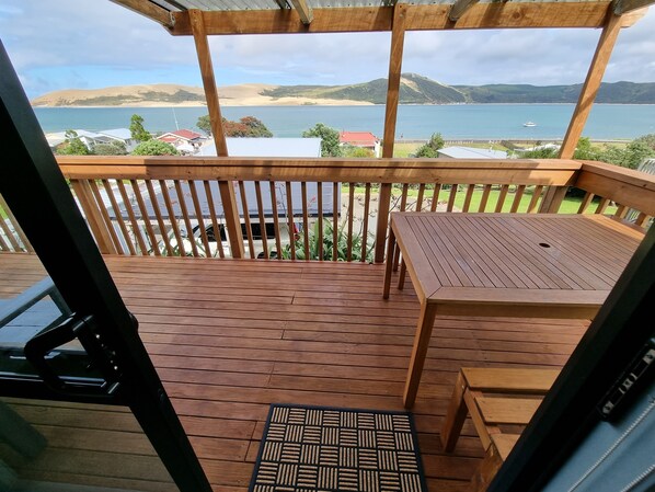 Een houten terras met een tafel en bankje, met uitzicht op een strand en heuvels.