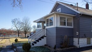 A two-story house with a front porch, a staircase leading to the second floor, and a small front yard with a bush and a stop sign visible in the background.