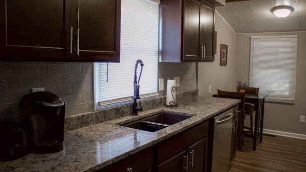 A kitchen with dark wooden cabinets, a granite countertop, a stainless steel sink, and a coffee maker.