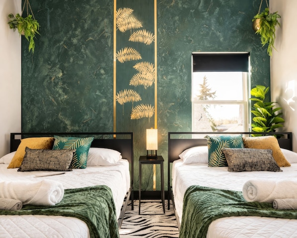A hotel room with two beds, a zebra-patterned rug, a green leaf wall decoration, and a window with a view of trees. - Overnight Gallery • The Art House • Near Downtown Dallas • Maduro Collection (Dallas)