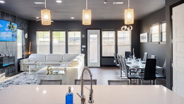 A modern kitchen with a central island, dining area with a long table and chairs, a sofa, and pendant lighting. - Overnight Gallery • The Art House • Near Downtown Dallas • Maduro Collection (Dallas)
