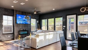 A modern living room with a sofa, TV, ceiling fan, and dining area. - Overnight Gallery • The Art House • Near Downtown Dallas • Maduro Collection (Dallas)