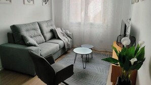 Ein modernes Wohnzimmer mit einem grauen Sofa, einem schwarzen Sessel, zwei kleinen runden Tischen und einem dekorativen Vogelkäfig mit weißen Blumen.