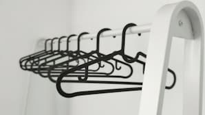 Ein weißer, metallener Kleiderständer mit mehreren schwarzen Kleiderbügeln vor einer weißen Wand.