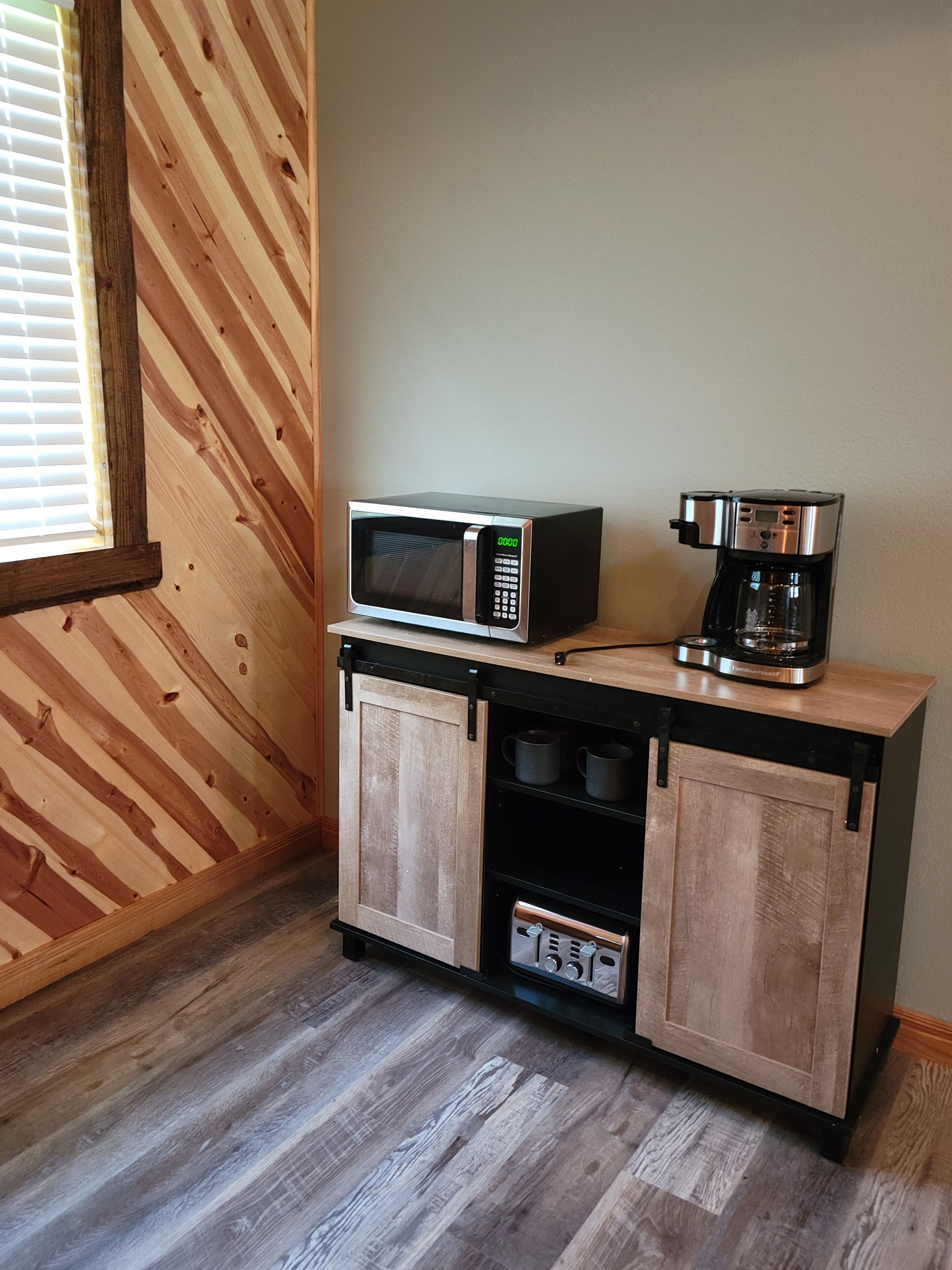 A kitchenette with a microwave and coffee maker on a wooden cabinet.