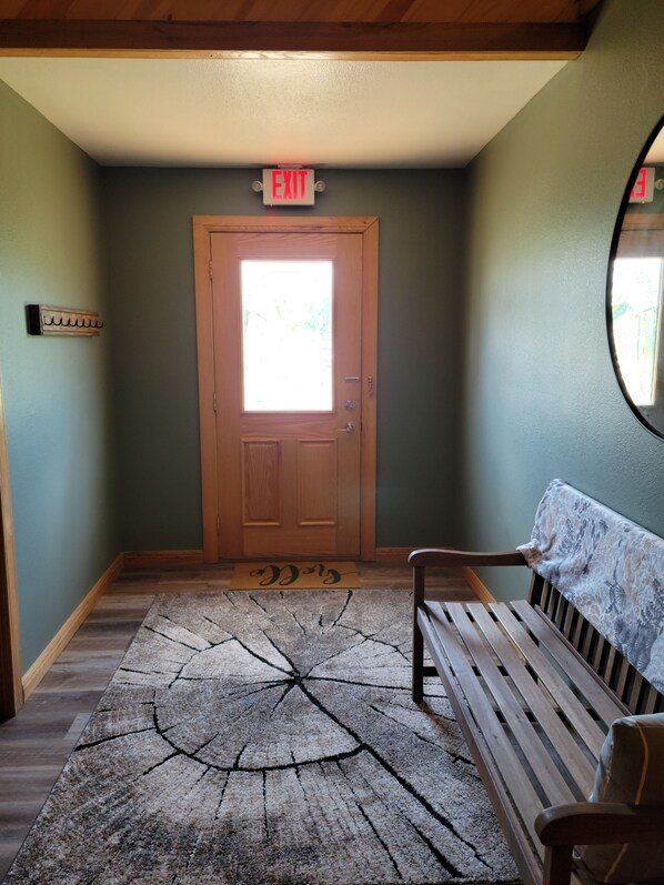 A hallway with a wooden bench, a door with an exit sign, and a patterned rug.