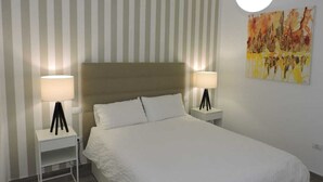 Una camera da letto ordinata con un letto grande, due comodini con lampade, una parete a righe e un quadro.