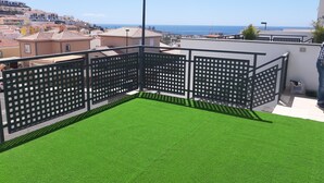 Una terrazza sul tetto con manto erboso sintetico, una recinzione in metallo e vista su una località costiera.