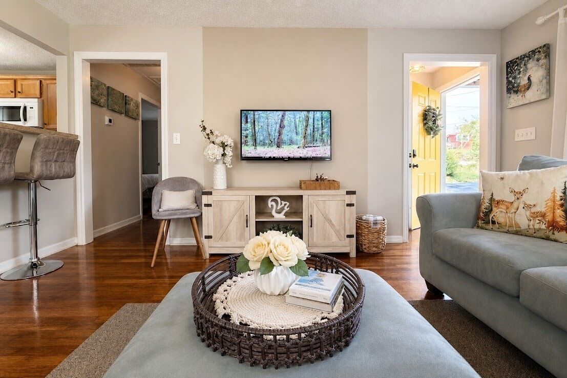 A living room with a television, a sofa, a coffee table with a vase, and a dining area with chairs and a microwave.