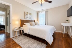 A bedroom with a bed, bedside table, lamp, ceiling fan, and a TV on a stand.