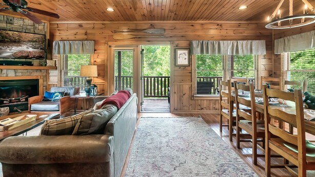A cozy cabin interior with a stone fireplace, wooden ceiling, and a dining area with a table and chairs. - Luxury Cabin between Pigeon Forge and Gatlinburg (Sevierville)
