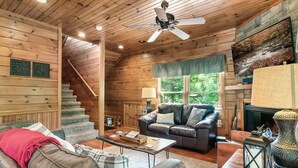 A cozy log cabin interior with a fireplace, leather sofa, and a staircase leading to the upper level. - Luxury Cabin between Pigeon Forge and Gatlinburg (Sevierville)