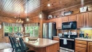 A modern kitchen with wooden cabinets, stainless steel appliances, and a central island with bar stools. - Luxury Cabin between Pigeon Forge and Gatlinburg (Sevierville)