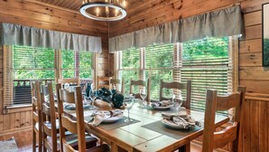 A wooden dining room with a large table set for four, surrounded by wooden chairs. - Luxury Cabin between Pigeon Forge and Gatlinburg (Sevierville)