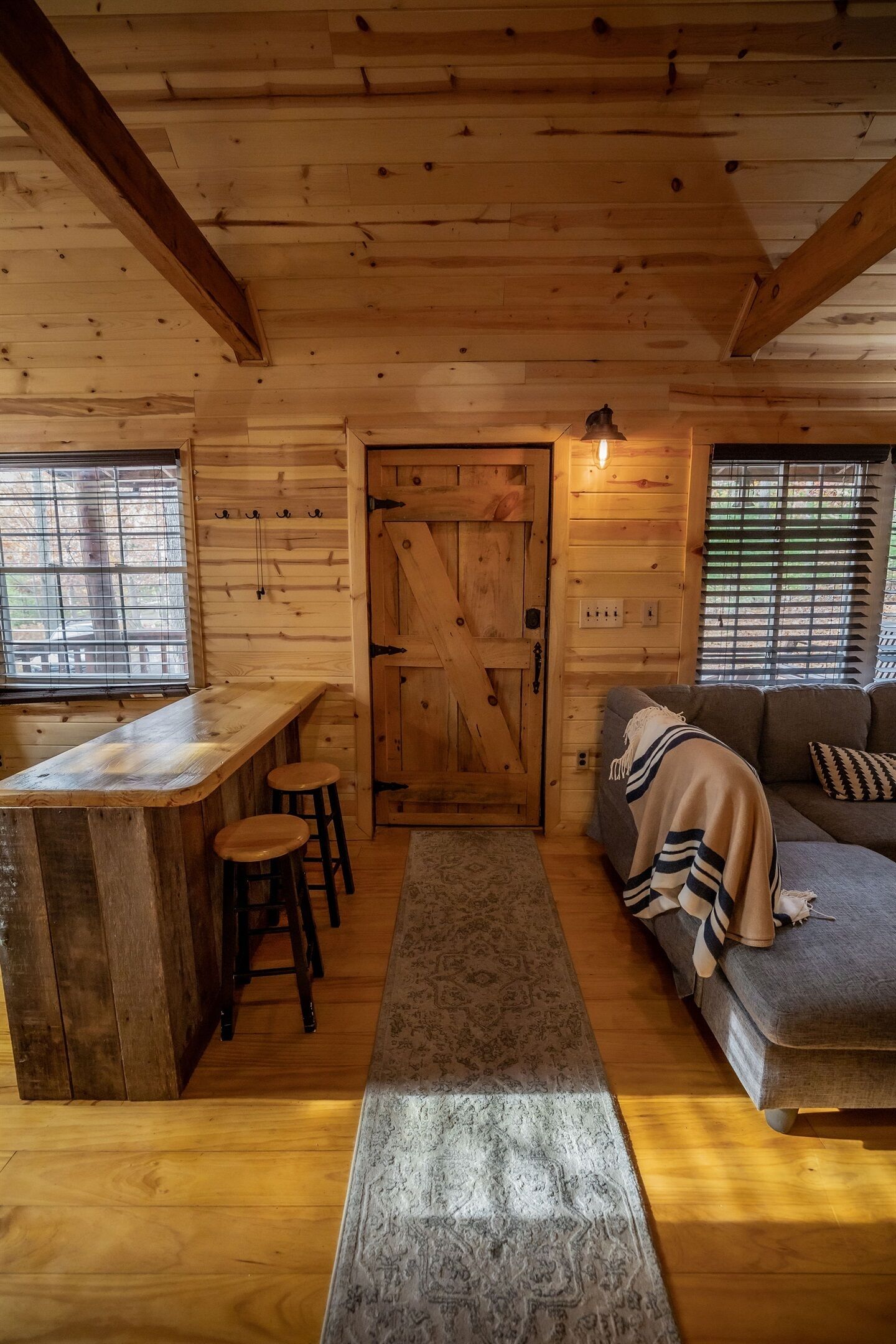 A wooden cabin interior with a bar area, a sofa, and a patterned rug.