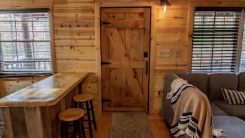 A wooden cabin interior with a bar area, a sofa, and a patterned rug.