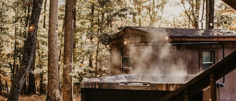Ein Whirlpool inmitten eines bewaldeten Geländes mit Holzbau und einer Treppe dorthin.