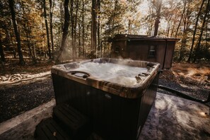 A hot tub in a forested area with a small cabin in the background. - Mountain Momma Hideaway (Upper Tract)