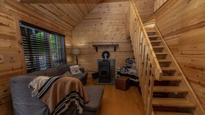 L’intérieur chaleureux d’un chalet avec un canapé, une couverture, une lampe, une cheminée et un escalier en bois.