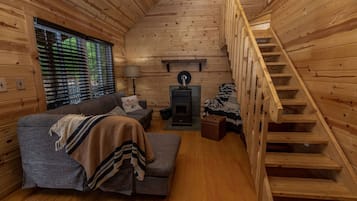 L’intérieur chaleureux d’un chalet avec un canapé, une couverture, une lampe, une cheminée et un escalier en bois.