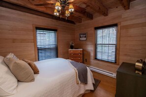 A bedroom with a bed, two windows with blinds, a dresser, a sign indicating a national forest reservation area, and a ceiling fan. - Mountain Momma Hideaway (Upper Tract)
