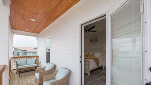 A wooden deck with wicker chairs and a bench, a bedroom with a bed and a ceiling fan, and a sliding glass door leading to the bedroom. - 🌴Luxury 4BR Beach Home🏖GULF VIEW🌊4 min Walk To The Beach (Panama City Beach)