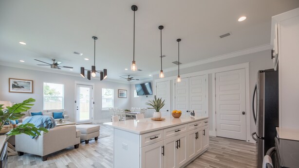 A modern kitchen with white cabinetry, a central island, pendant lighting, and a built-in TV. - 🌴Luxury 4BR Beach Home🏖GULF VIEW🌊4 min Walk To The Beach (Panama City Beach)
