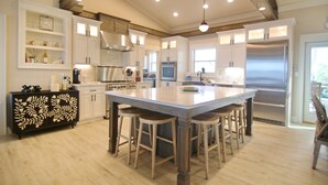 A spacious kitchen with a large island, wooden bar stools, white cabinetry, and stainless steel appliances. - Bayfront, Pool, Pier, 2 Hot Tubs!, Sandy Beach, Private, steps from beachfront (Saint George Island)