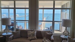 A cozy living room with a large window overlooking a pier and the sea. There are two lamps on side tables and a sofa with cushions. - Bayfront, Pool, Pier, 2 Hot Tubs!, Sandy Beach, Private, steps from beachfront (Saint George Island)